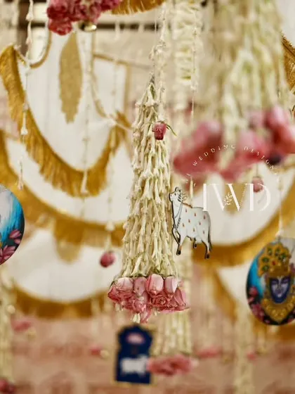 Detailed hanging decor from a spiritual event, featuring pichwai-style paintings of Lord Krishna and other traditional motifs mixed with fresh flower strings.