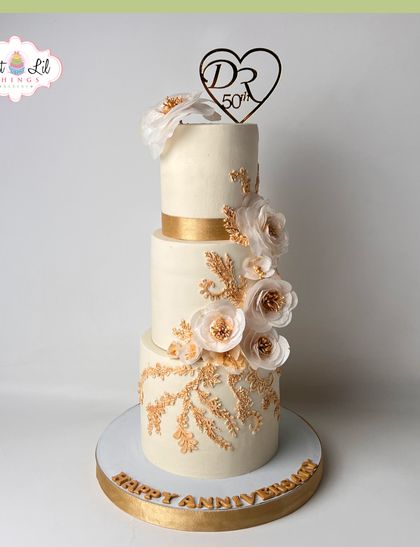 A grand three-tiered cake for a 50th golden anniversary. This elegant creation is adorned with a cascade of handcrafted golden flowers and intricate gold detailing.