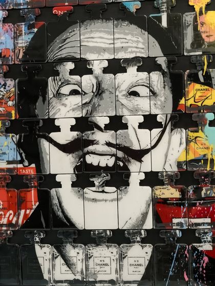 A close-up of "Dali In A Bottle," focusing on the artist's unmistakable grin piercing through the grid of luxury and consumer brands.