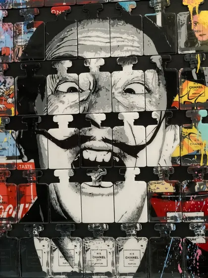 A close-up of "Dali In A Bottle," focusing on the artist's unmistakable grin piercing through the grid of luxury and consumer brands.