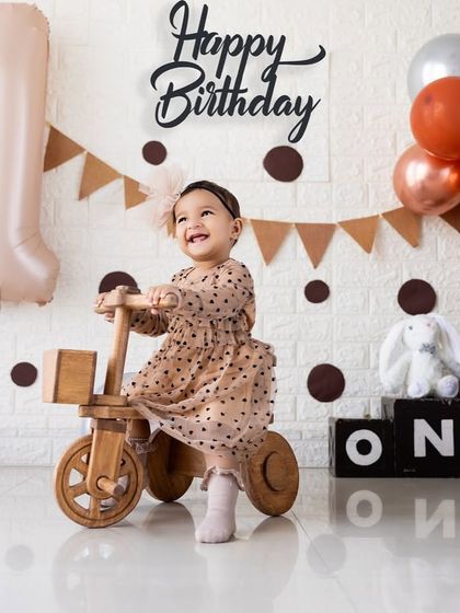A joyful smile from the birthday girl on her wooden tricycle. This rustic-themed first birthday shoot uses natural props and a neutral color palette.