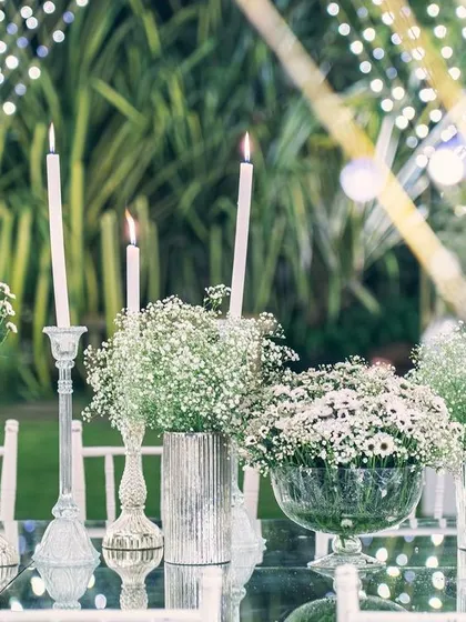 A tablescape detail from the sangeet, where candles and delicate white flowers create a soft, romantic glow. The background of twinkling lights adds to the enchanting atmosphere.