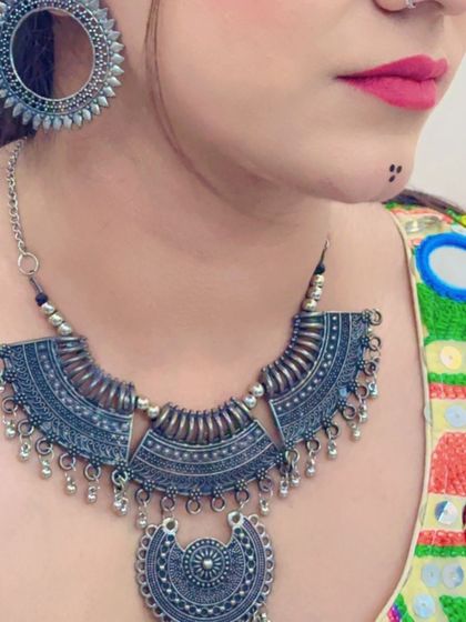 A large, statement oxidized silver necklace with intricate patterns and chain tassels.