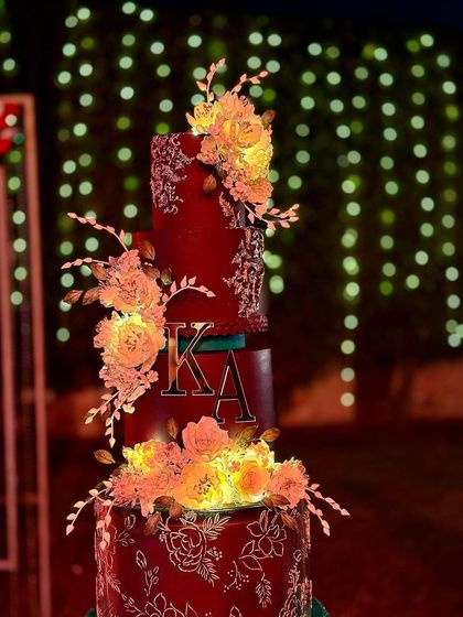 A full view of our first wedding cake in Delhi, a special creation for a special couple. The deep red and green tiers are adorned with hand-painted details and lit-up sugar flowers.