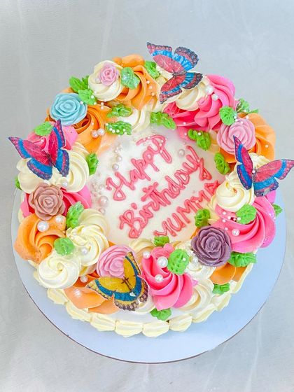 A beautiful floral wreath cake for a special mummy. The combination of orange, pink, and white roses with delicate butterflies creates a stunning and heartfelt design.