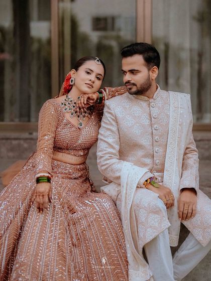 The couple seated together, sharing a moment of quiet connection. The bride's intricate lehenga and the groom's classic sherwani are beautifully detailed.