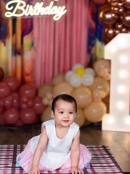 The birthday girl crawling on a mat, with a large light-up number '1' and festive balloons in the background.