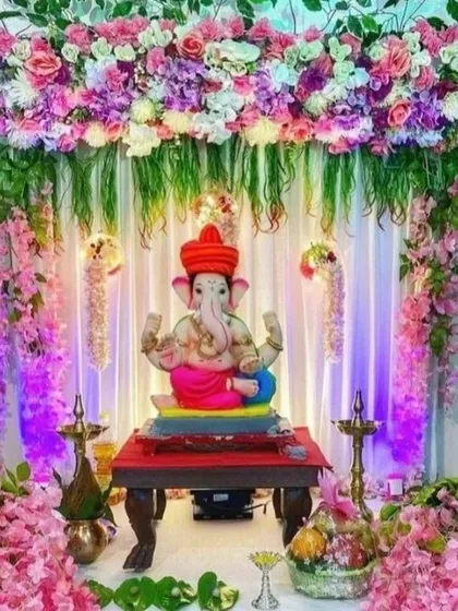 A lovely pink-themed Ganpati decoration with cherry blossom branches and a floral arch. The soft lighting and delicate flowers create a calm and peaceful ambiance.