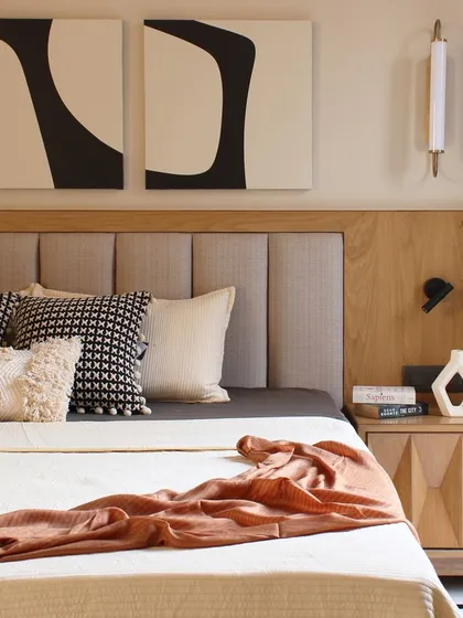This bedroom in the Jaipur House is designed as an inviting retreat. A mix of textures, from the upholstered headboard to the patterned cushions, creates a cozy sanctuary that feels uniquely personal.