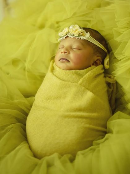 A monochrome look with a bright lime green. The baby wears a matching floral headband and is wrapped in a soft swaddle against a textured tulle background.