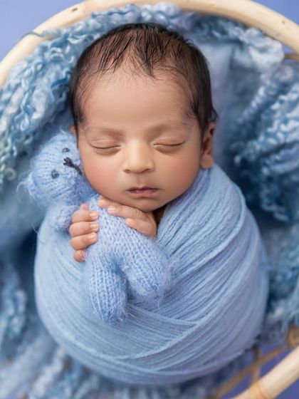 A close up of a baby boy swaddled in blue, holding a tiny knit teddy bear. This shot emphasizes the comfort and security that a swaddle provides.