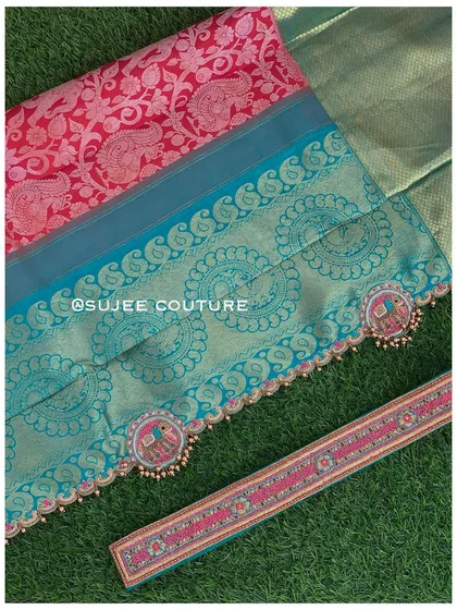 A detailed flat-lay of a half saree set. This shows the rich red and blue fabrics, the custom embroidered vaddanam, and the elephant-motif tassels designed for the dupatta.