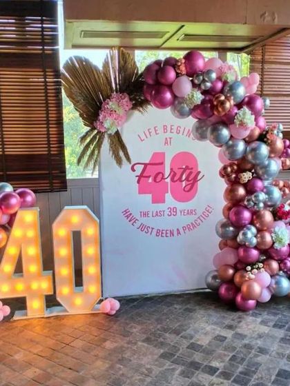 A chic 40th birthday party with the theme "Life Begins at Forty." This decoration includes a beautiful pink, silver, and rose gold balloon arch, a custom backdrop, and large light-up marquee numbers.