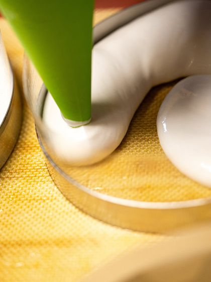 Piping a smooth, white meringue into a ring mold. This is a foundational step for many advanced desserts taught in our masterclasses.