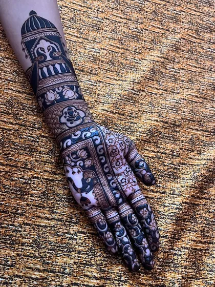 This full-hand design showcases a variety of motifs, including a doli, Ganesha, elephants, and lotus flowers, creating a rich tapestry of symbols.