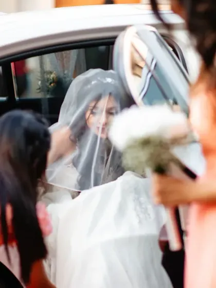 The bridesmaids help the bride with her dress as she gets out of the car, a moment of motion and support.