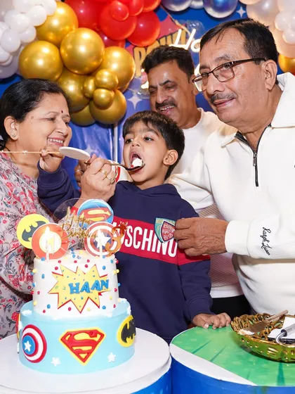 Grandparents lovingly feeding the birthday boy his first bite of the superhero-themed cake. We create celebrations that bring the whole family together for these heartwarming moments.
