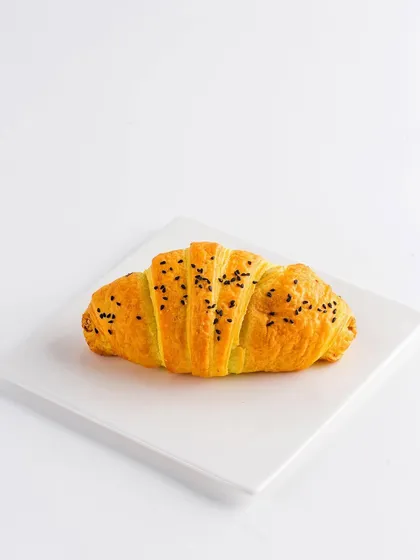 A single, perfect croissant on a white plate. This minimalist, high-key photograph is ideal for catalogues or menus, focusing entirely on the pastry's flaky layers and golden color.