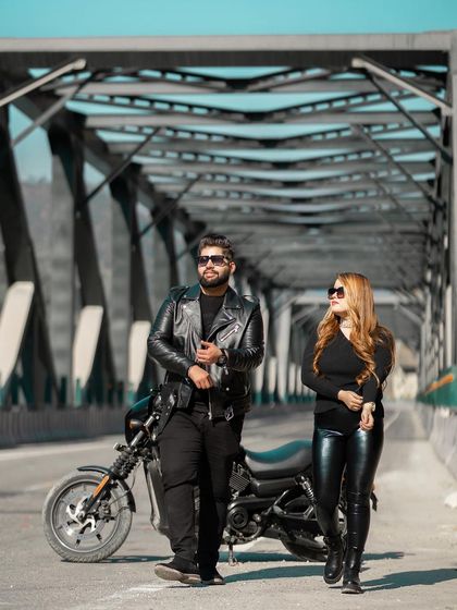 A full-length shot of the couple with their motorcycle on a bridge, capturing their cool and contemporary style. This is a great example of a themed pre-wedding shoot.