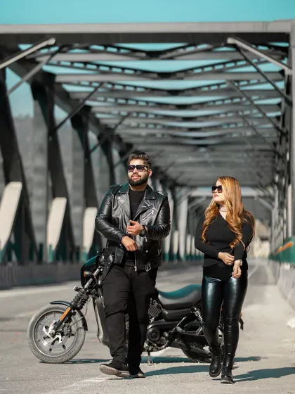 A full-length shot of the couple with their motorcycle on a bridge, capturing their cool and contemporary style. This is a great example of a themed pre-wedding shoot.