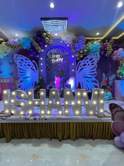 A beautiful butterfly theme for Ishanni's birthday. The stage features large, illuminated butterfly wings, a purple shimmer wall, and a pastel balloon arch with gold highlights.