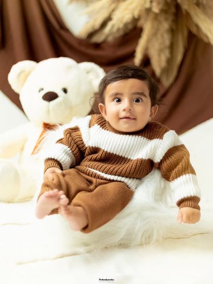 A full-length portrait of a baby boy in a comfy knit outfit, showing off his tiny feet.