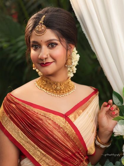 Portraits from a makeup shoot, showcasing a model in a classic red and cream saree. The images highlight the flawless makeup and traditional styling in a beautiful garden setting.