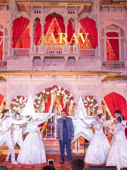 The groom makes his dashing entry for the 25th-anniversary function. He is surrounded by dancers holding star-shaped props against the stunning facade of Chomu Palace.