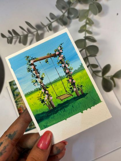 Holding up my polaroid painting of a floral swing. I love how the pink roses pop against the green field and blue sky in this little gouache scene.