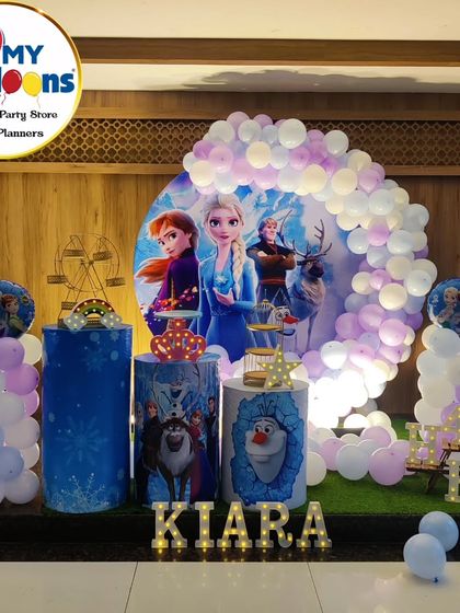A magical Frozen-themed fourth birthday party. The setup features an Elsa and Anna backdrop, a purple and white balloon arch, and an 'Olaf' plinth.