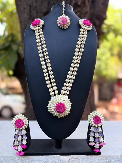 A beautiful floral set on display. This includes a necklace, maang tika, and jhumkas, all made with mogra buds and a combination of pink and purple flowers.
