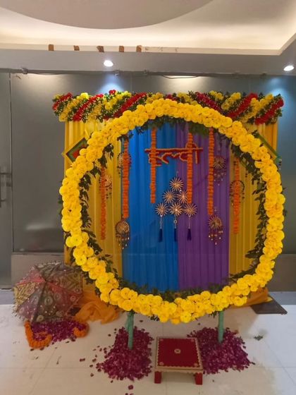A colorful Haldi setup with a circular marigold backdrop. The decor includes a small stool for the ceremony, Rajasthani umbrellas, and a floor scattered with rose petals.