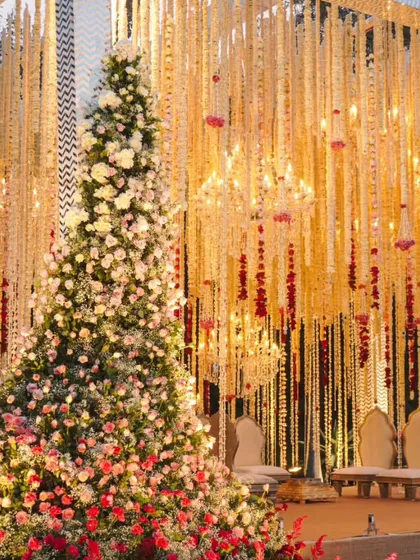 A symphony of blossoms. This wedding stage features a massive floral tree installation next to a backdrop of cascading white and red flowers, creating an enchanting and opulent look.