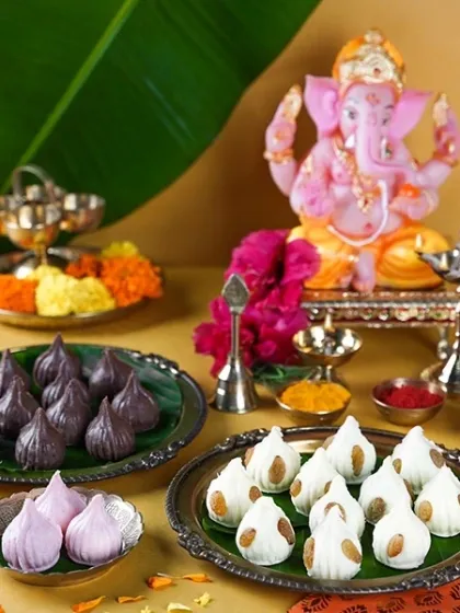 A variety of colorful modaks, including traditional white, purple, and black versions, arranged as an offering to a pink Ganesha idol. This shot celebrates both tradition and innovation.