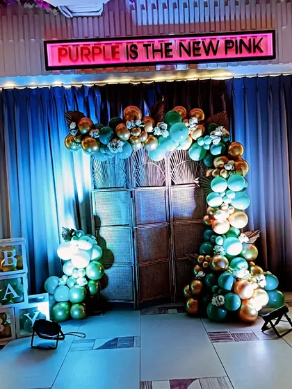 A bold and unconventional baby shower theme with the sign "Purple is the New Pink". The green and gold balloon arch against a rustic backdrop offers a stylish and edgy alternative to traditional colors.