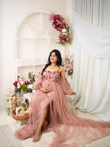A full-length portrait of the mother-to-be, looking radiant and hopeful. The flowing pink gown and bright, airy setup create a dreamy and ethereal look.
