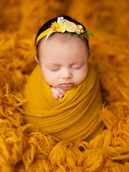 A peaceful portrait of a baby in a mustard yellow wrap, adorned with a delicate floral headband. The warm tones are so comforting.