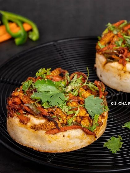 Our Kulcha Bun is an open-faced savory bun topped with a mix of spiced vegetables and fresh coriander. It's a hearty and flavorful snack.