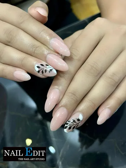 A simple yet beautiful design featuring a sheer nude base on almond nails, with two accent nails adorned with hand-painted black leafy branches.