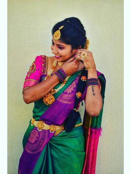This client is styled in a beautiful green and pink silk saree with pearl and temple jewelry. The makeup is kept elegant with a focus on defined eyes and glowing skin.