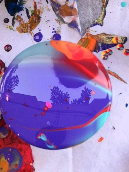 A glossy, freshly poured coaster reflecting the trees outside. The smooth, glass-like surface is a signature of a well-done acrylic pour.