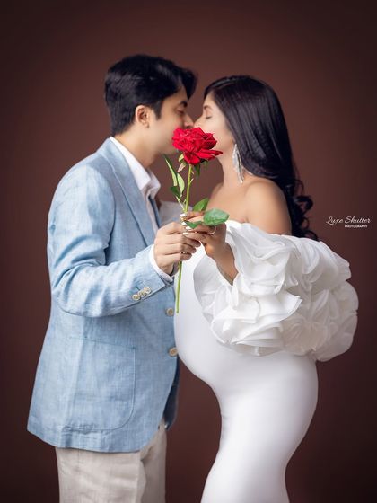 A romantic and playful moment as the couple shares a kiss over a red rose. It's a sweet way to add a classic symbol of love to your maternity photos.
