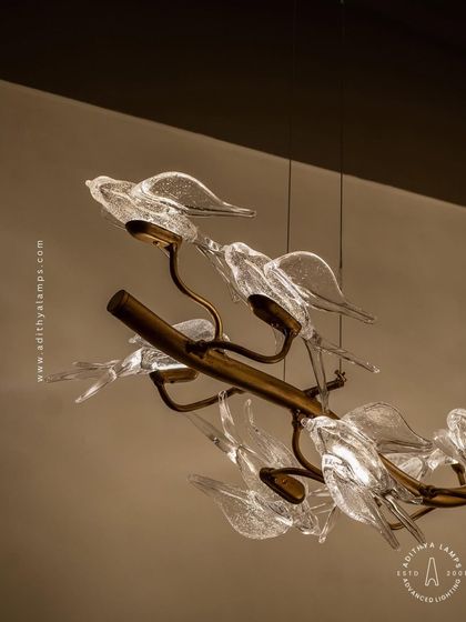 This horizontal chandelier features a flock of glass birds perched on a branch, as if in mid-flight. It's a perfect statement piece for suspension over a long dining table or in a living room, adding a dynamic and natural element.