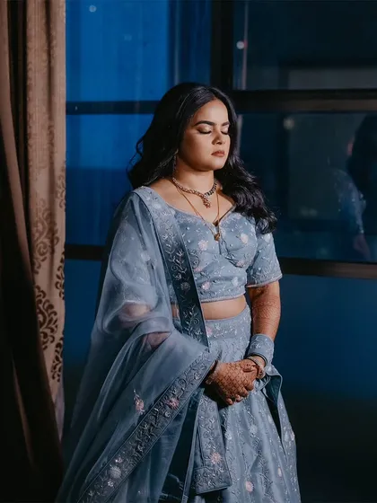 A serene portrait of the bride at her reception, standing by a window with cool blue light creating a calm, contemplative mood.