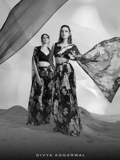 A black and white artistic shot of two models in floral printed ensembles, showcasing the flow and form of the designs.