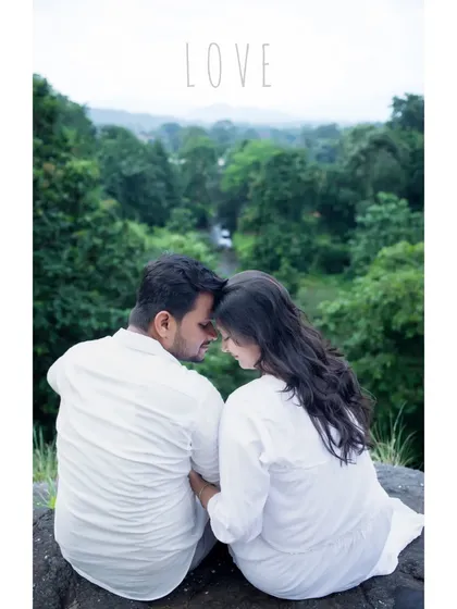 An intimate and romantic maternity portrait of a couple dressed in white, sitting together overlooking a lush green valley. This quiet moment, with their foreheads touching, beautifully captures the love and serenity of their journey together.