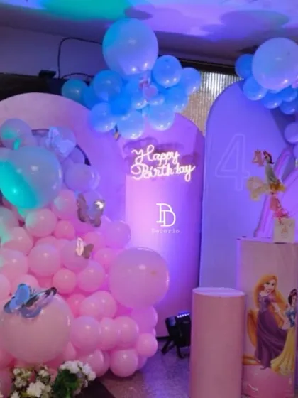 A Disney princess-themed party for a 4th birthday, featuring characters like Snow White and Rapunzel. The setup uses purple and pink backdrops, themed pedestals, and soft balloon colors to create a royal celebration.