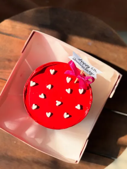A shiny red glaze bento cake for a 4th anniversary, decorated with white hearts and a little bow.