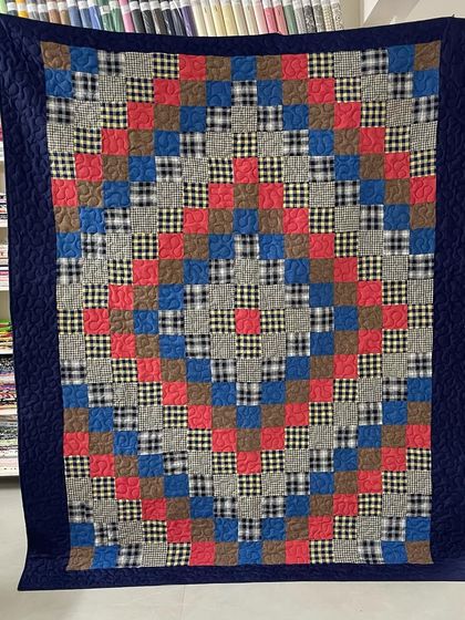 A cozy memory quilt made from plaid and solid-colored shirts, arranged in a classic checkerboard pattern with a dark blue border.