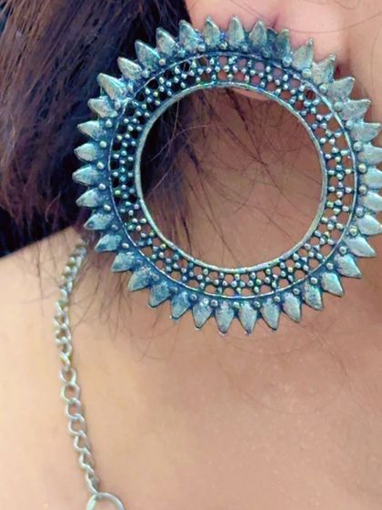 A large, circular oxidized silver earring with a sunburst design, perfect for making a statement.